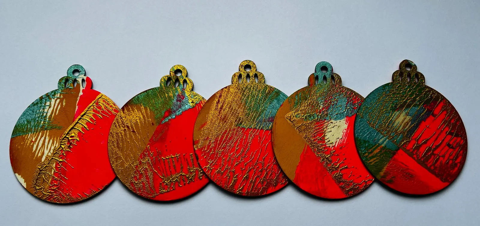 Five rounded wooden ornaments with vivid red, teal and gold gelli print.