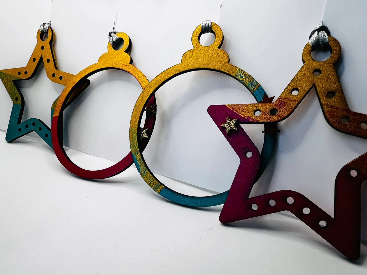 Open circular and star-shaped hanging forms in ochre, teal, red and magenta.